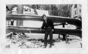 old black and withe photo of young man standing in front of two wooden canoes
